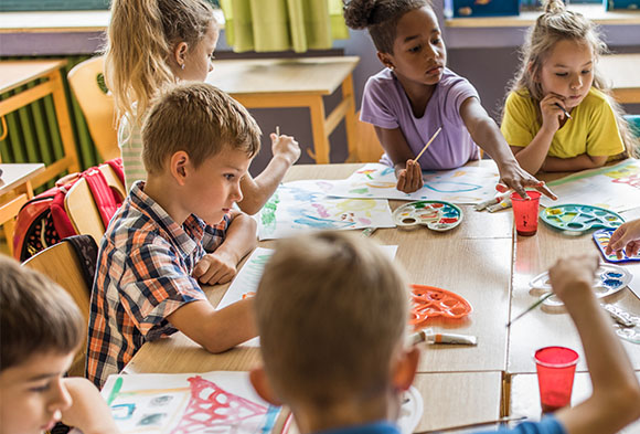 A group a young children painting at their desks.